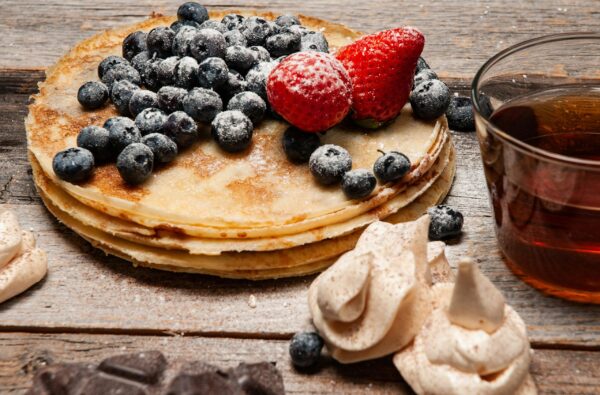 Stack of homemade pancakes topped with fresh blueberries and strawberries, served with syrup.